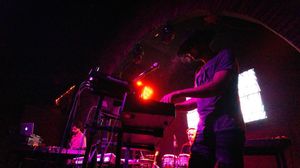 Performers on stage in a dimly lit venue with red and purple lighting creating a moody atmosphere.