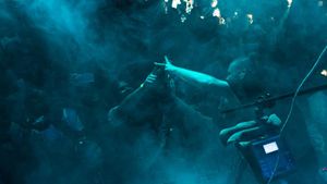 Concert performer silhouetted against atmospheric blue lighting and smoke effects.