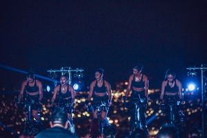 Indoor cycling class at night with city lights visible in background.