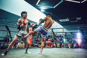 Two fighters exchange strikes during an intense kickboxing match in a brightly lit ring.