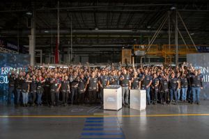 Large group photo of employees gathered in industrial warehouse space for company event.