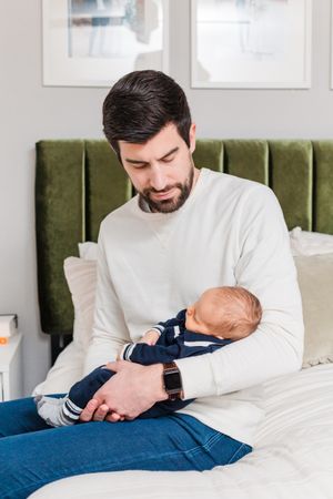 father holding newborn baby on bed