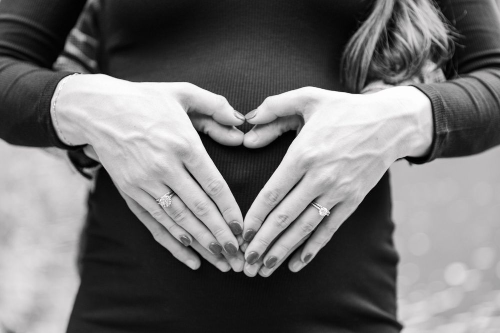 black and white expecting mom and dad forming heart hands on belly