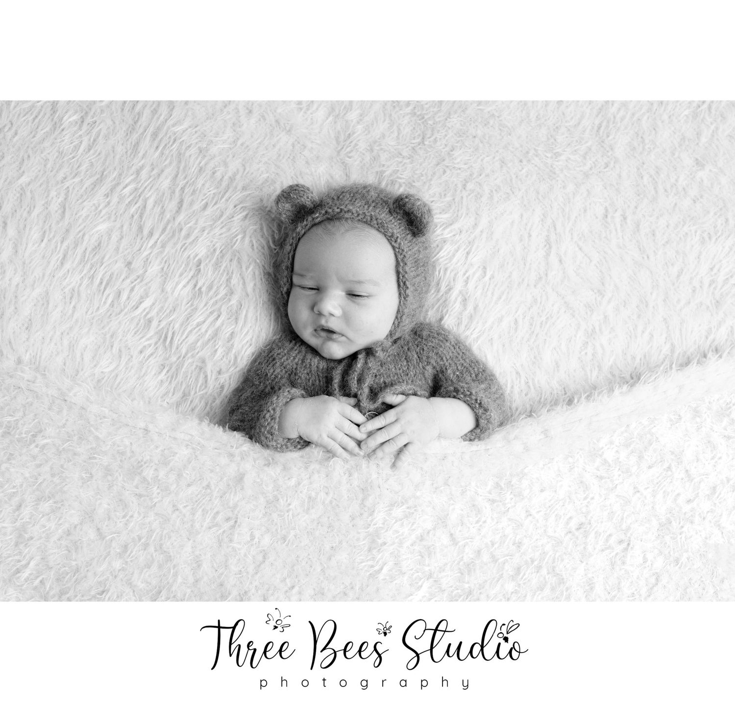 Black and white portrait of baby wearing fuzzy bear hood on white background.