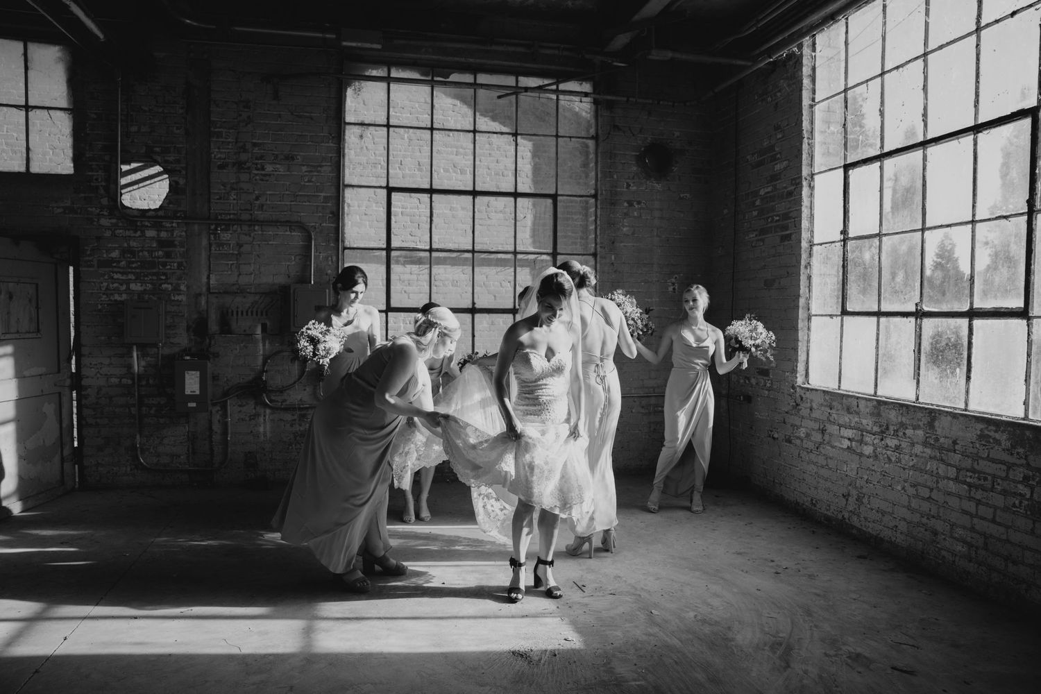 Black and white photo of people dancing joyfully in an industrial loft space with large windows.