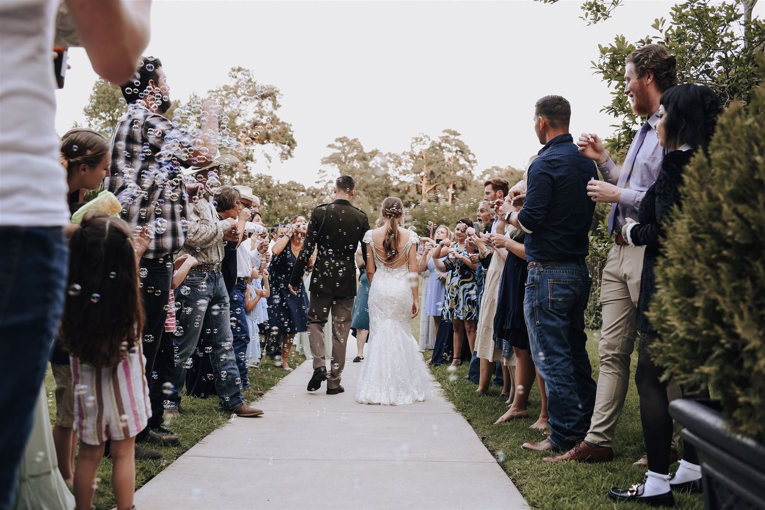 Guests line a pathway outdoors as newlyweds walk through during a wedding celebration.