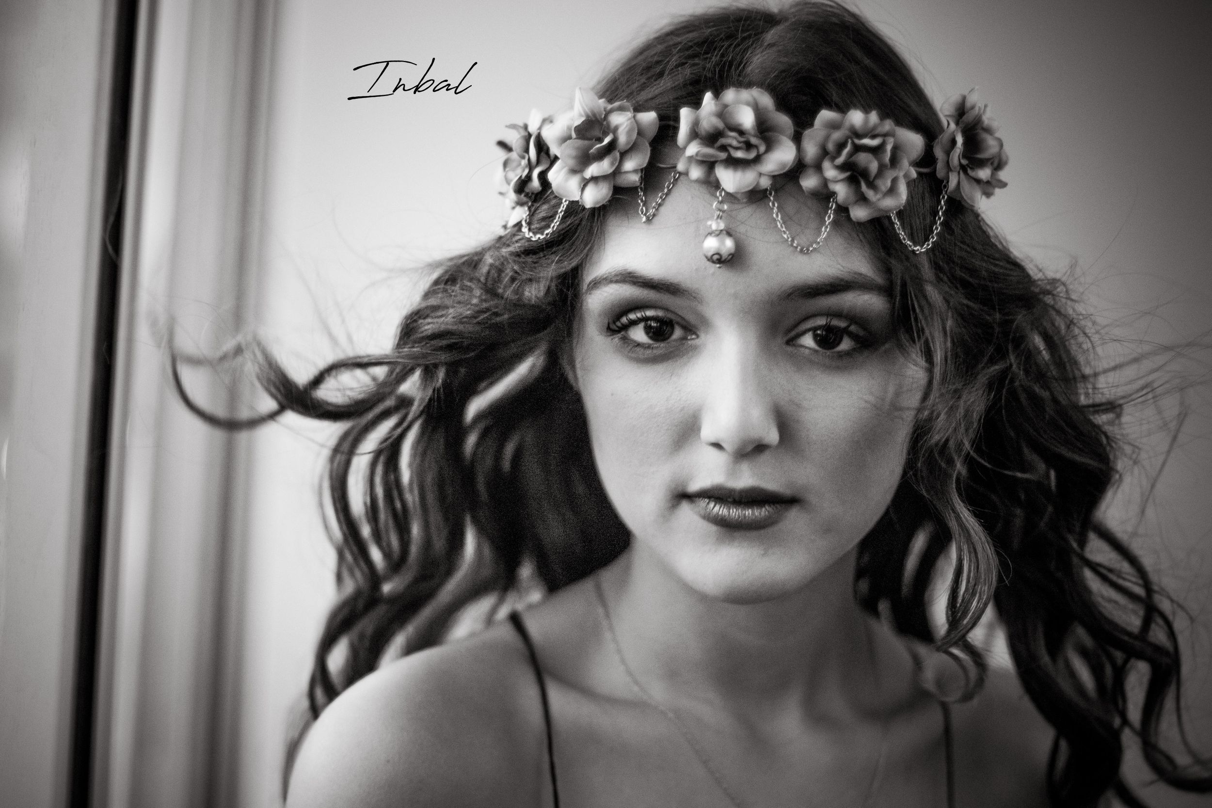 Black-and-white photo of a teenager with long curly waving hair with flower crown on her head.