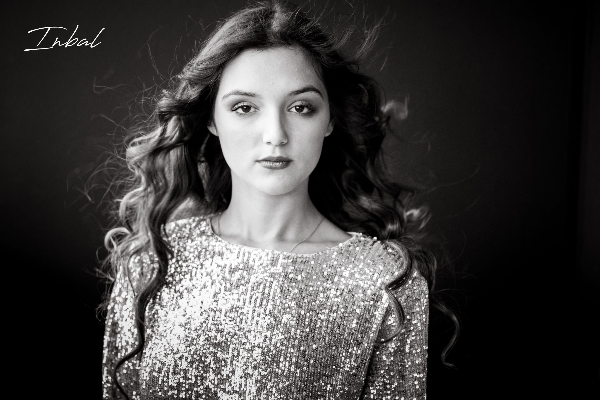 Black-and-white photo of a teenager with long curly waving hair looking at the camera.