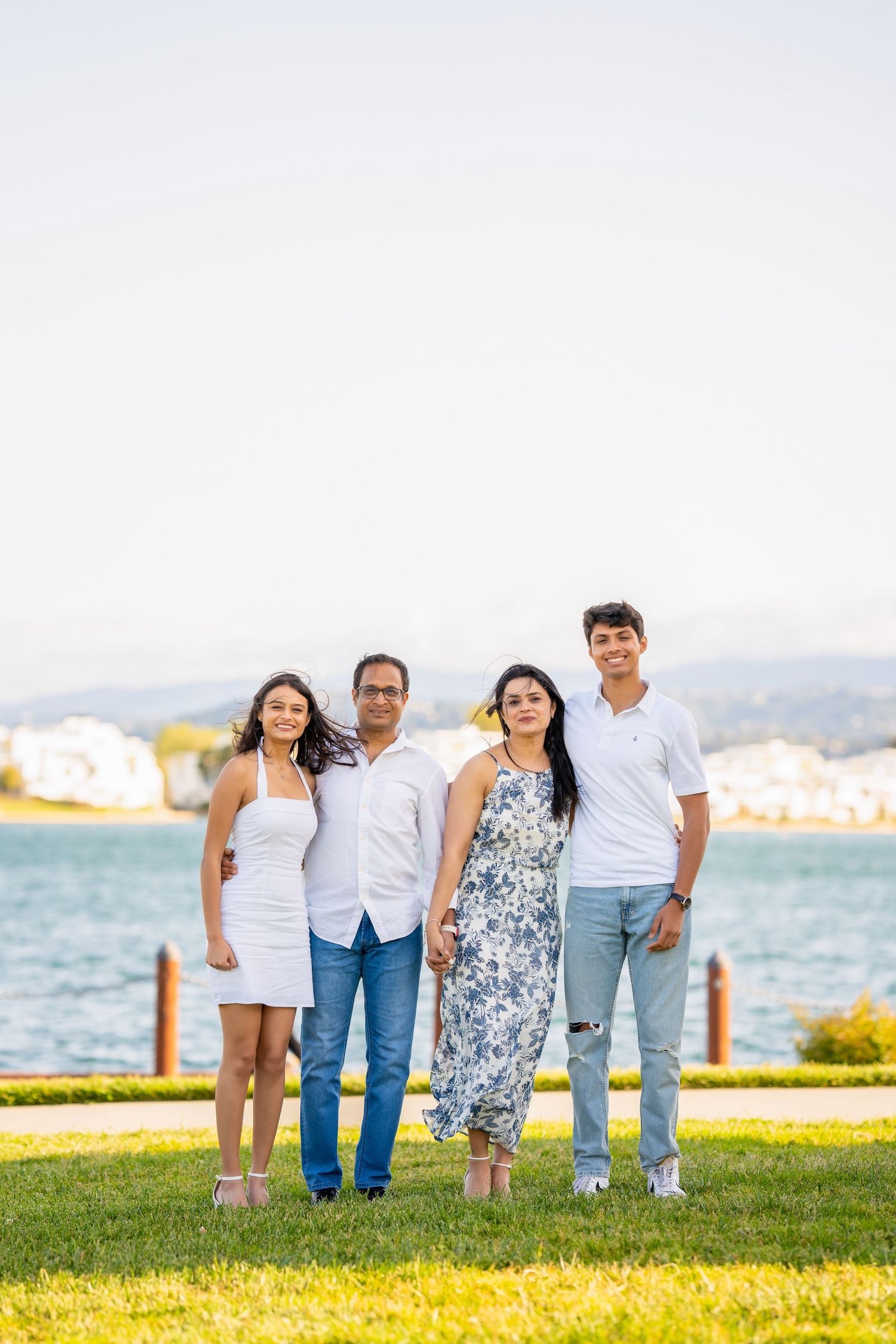 Family of four poses by waterfront with city view in background during golden hour.