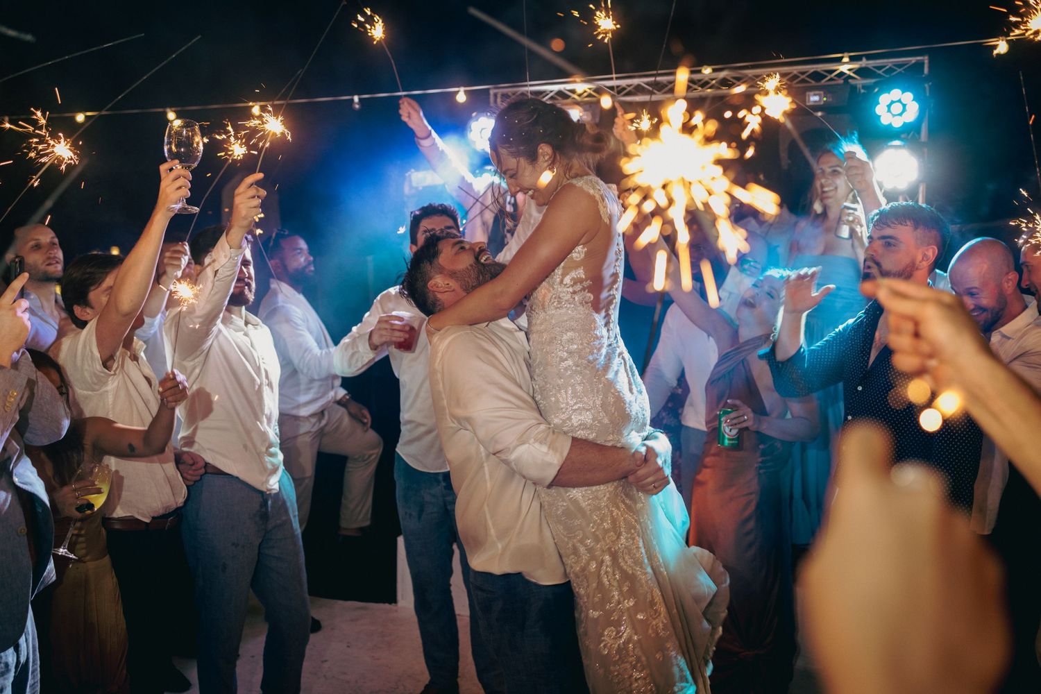 Wedding party dancing and celebrating with sparklers in a dimly lit reception.