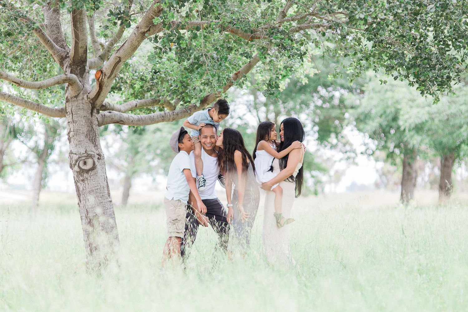 Family enjoying a relaxed photo session in a dreamy meadow under large trees.