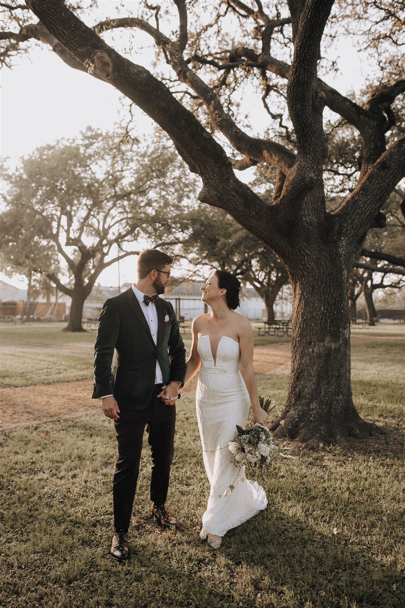 A couple walks hand in hand under a grand oak tree during their wedding.