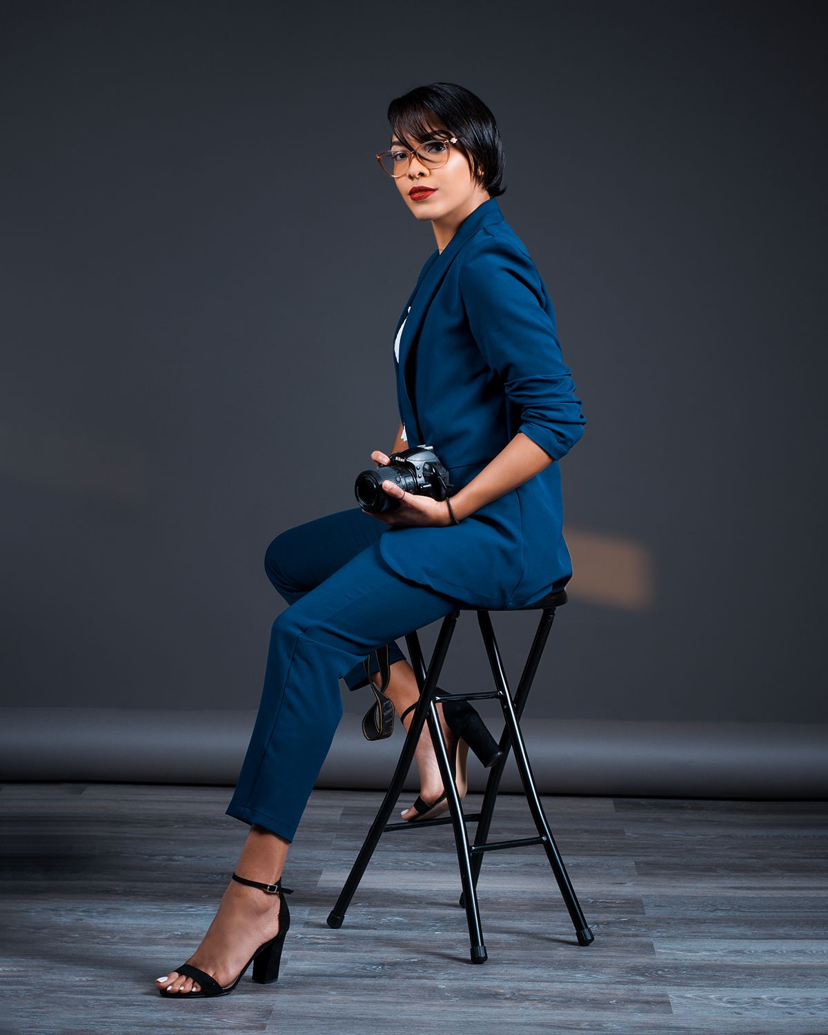 Personal branding photography in Allentown PA of professional woman in blue suit sitting on stool holding camera.