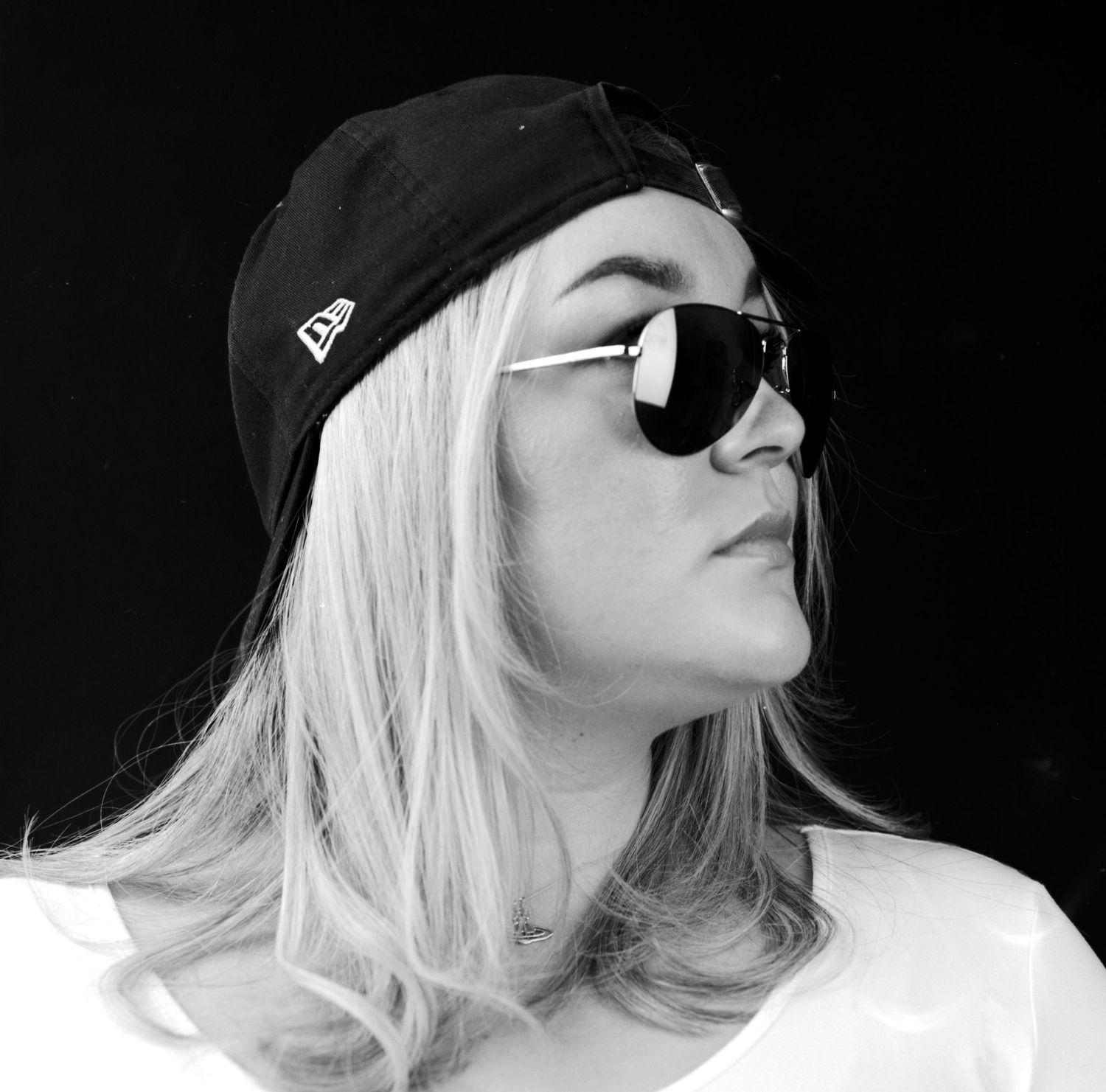 Black and white head and shoulders portrait photograph of young lady wearing sun glasses and a cap in the studio