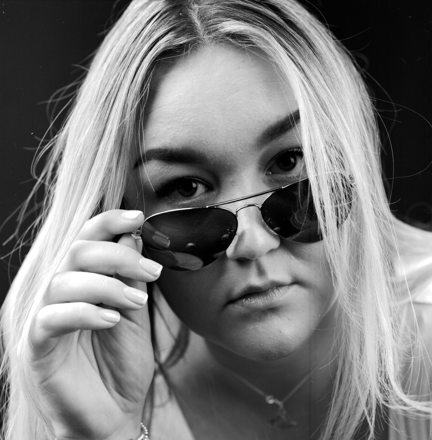 Black and white head and shoulders portrait photograph of young lady wearing sun glasses captured in the studio