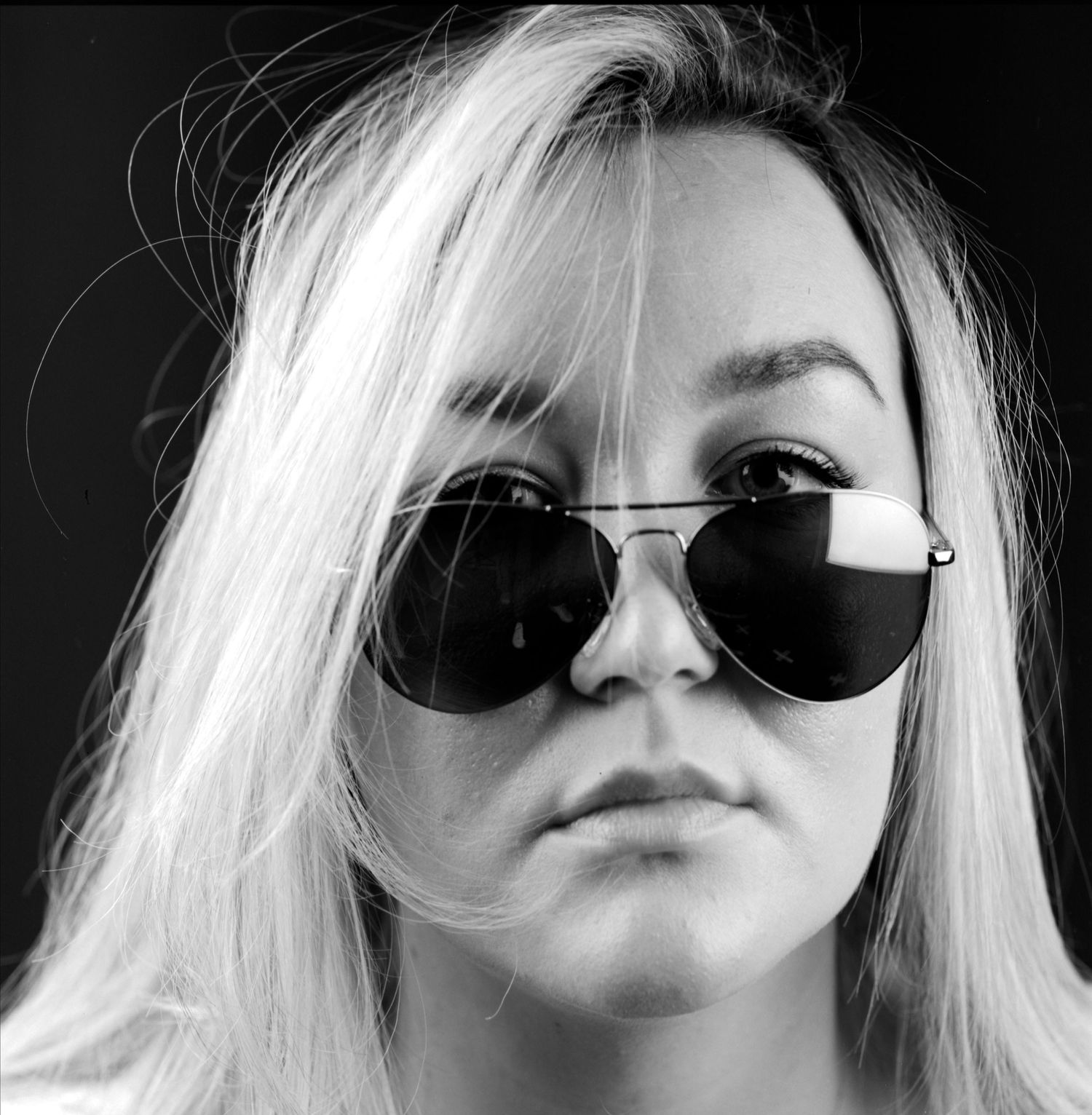 Black and white head and shoulders portrait photograph of young lady wearing sun glasses captured in the studio