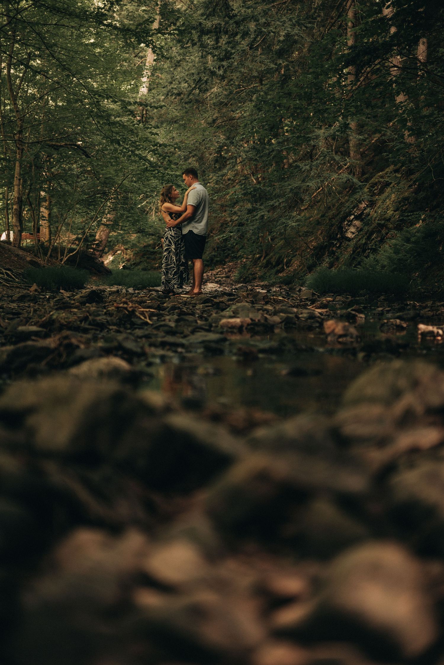 A romantic moment captured on rocky terrain with a misty forest background.