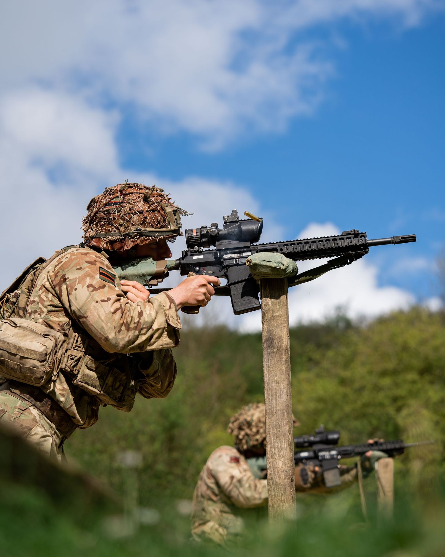 Military personnel conduct rifle training exercises in outdoor terrain.