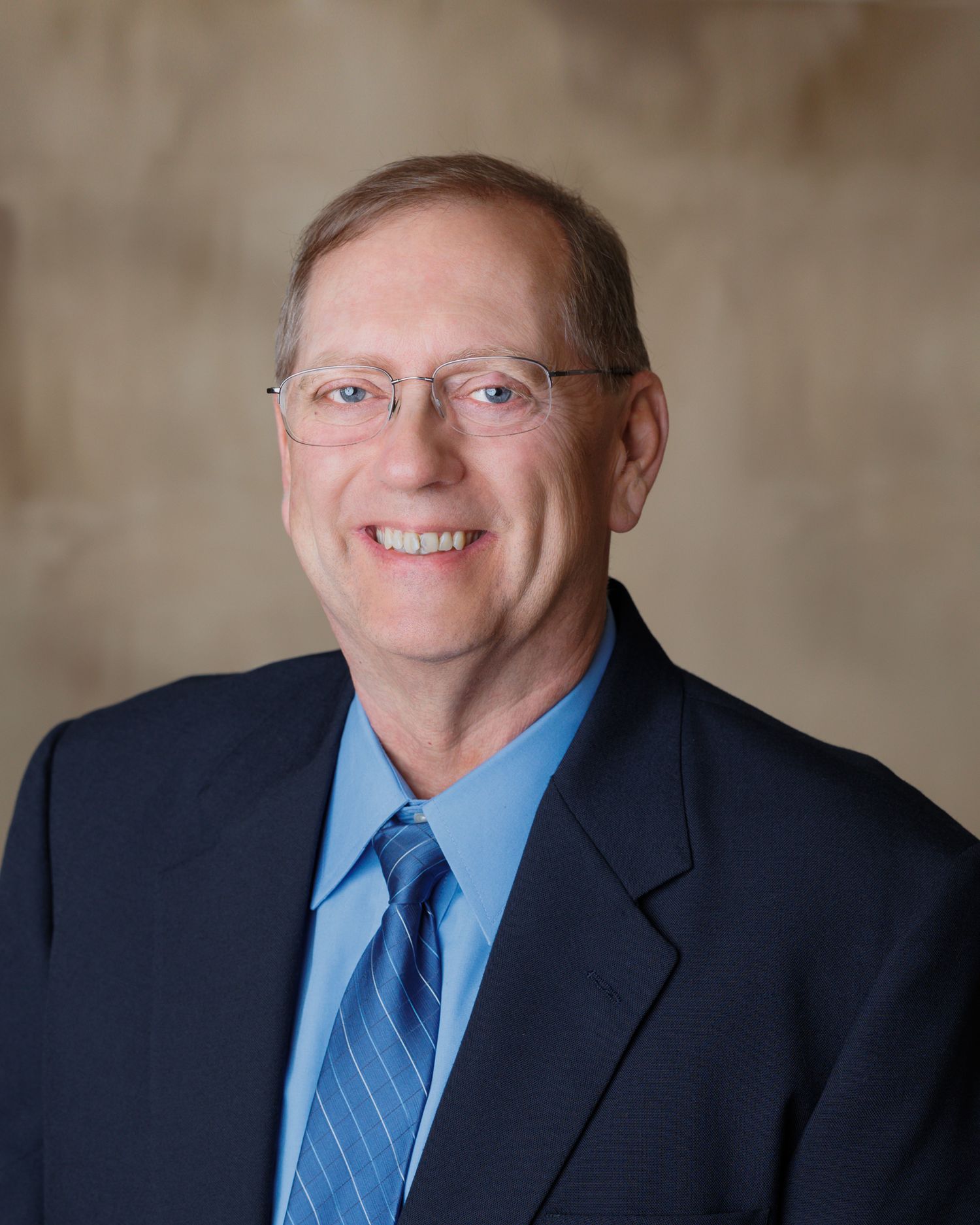 Professional portrait of a person in a navy suit and blue tie.