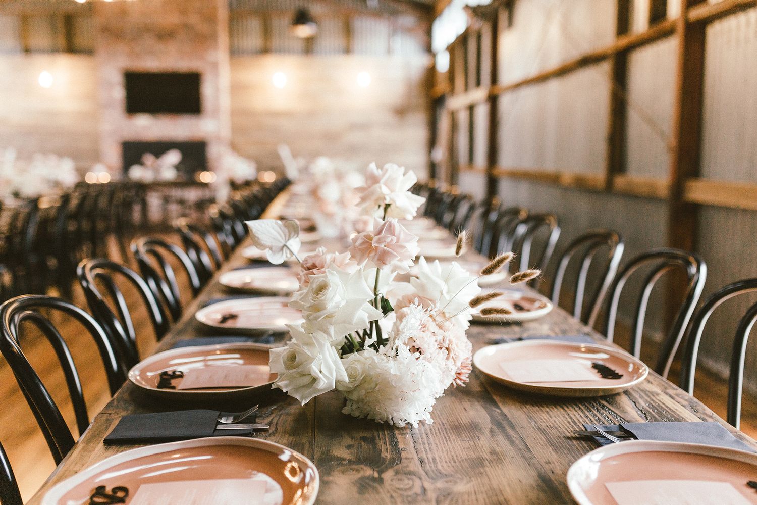 Long farmhouse tables decorated with white flowers and place settings for wedding reception.