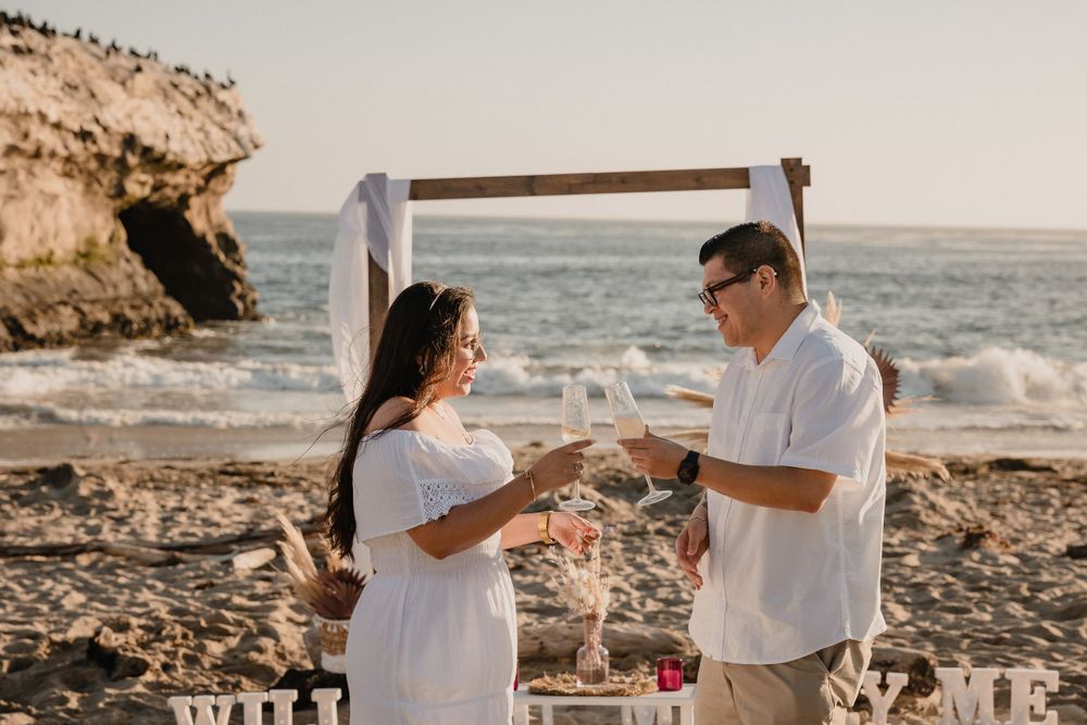 A couple exchanges rings during their beach ceremony next to a decorated wooden arch.