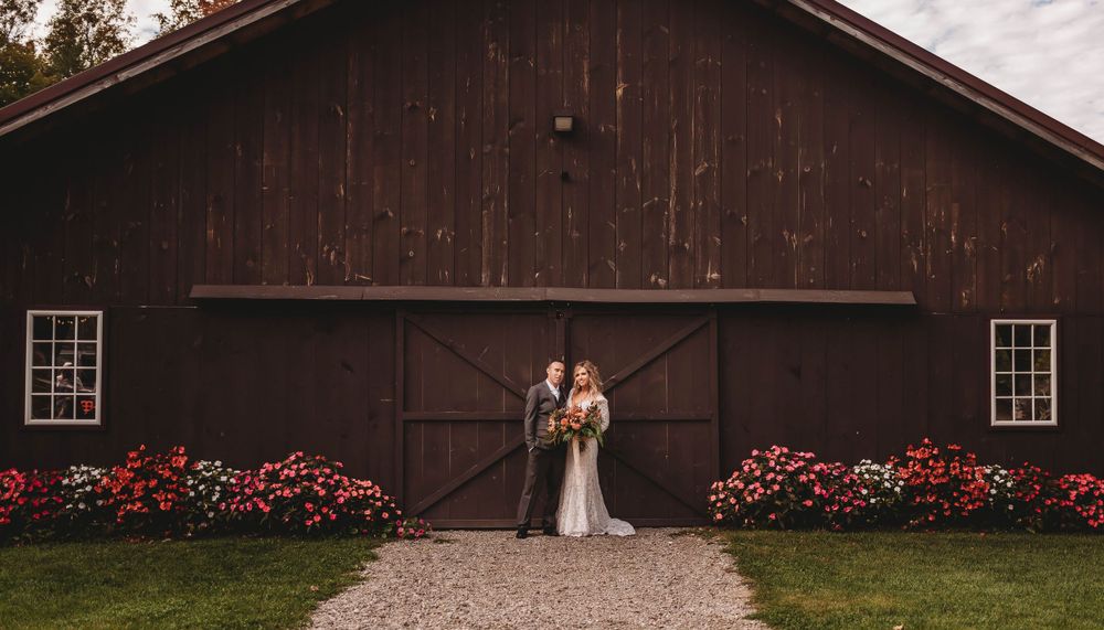 A rustic barn wedding scene with red flowers lining the entrance path on a cloudy day.