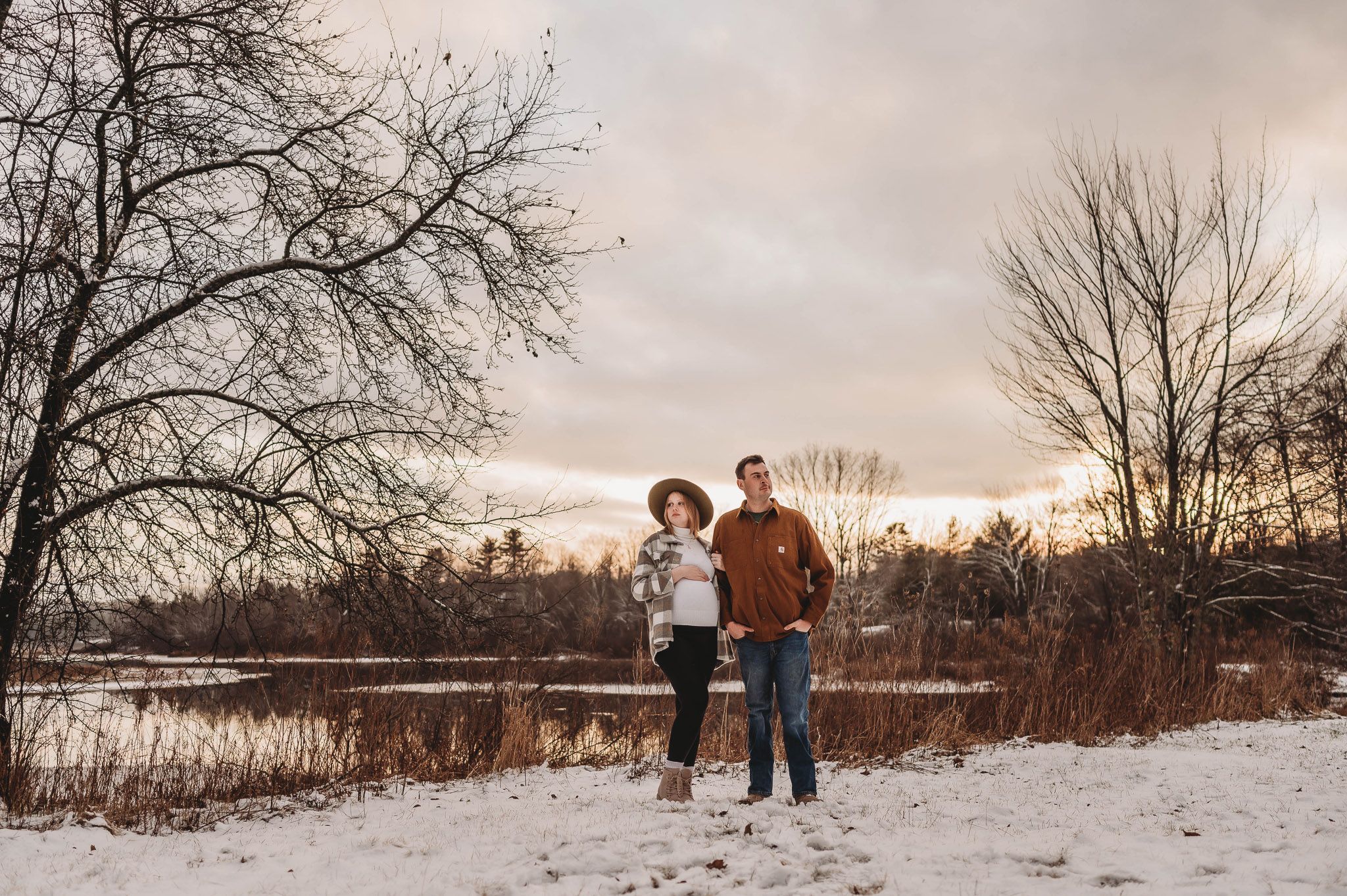 A winter landscape photo of figures walking through snow-covered ground at sunset.