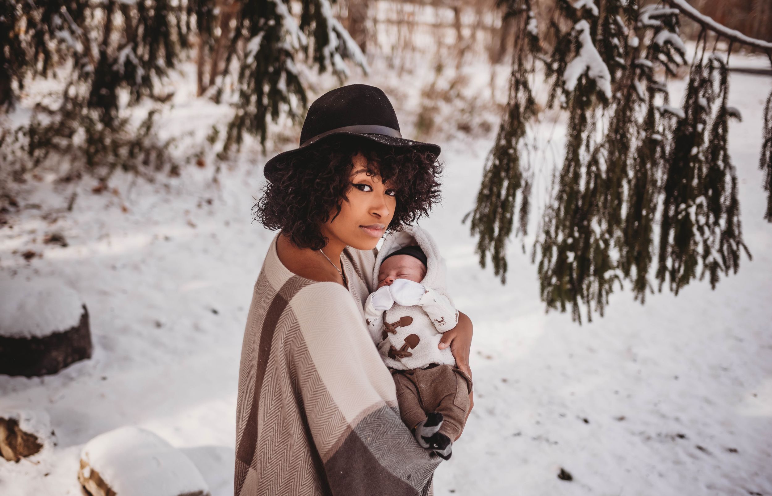 Person in a wide-brimmed hat holds a small dog while standing in a snowy winter landscape.