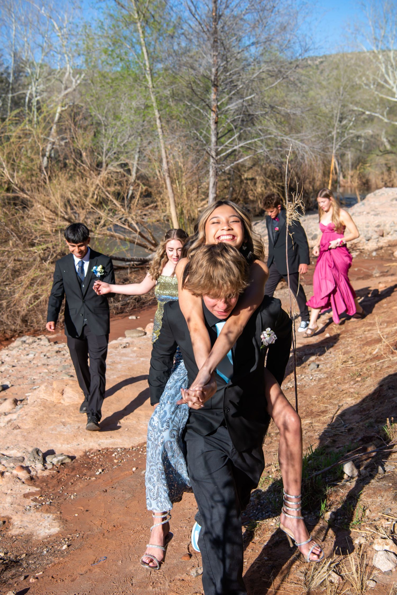 Wedding party playfully walks along a dirt trail in a natural outdoor setting. Senior Portraits
