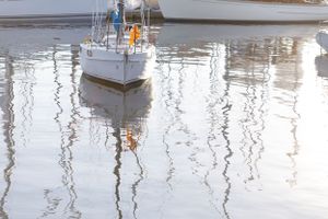 White sailboat reflected in calm harbor waters creating symmetrical ripple patterns.