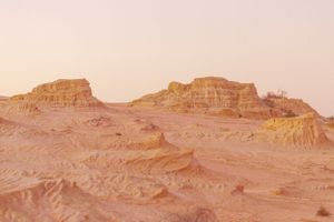 Rocky desert landscape with rusty orange mesas and cliffs under pink sunset sky.