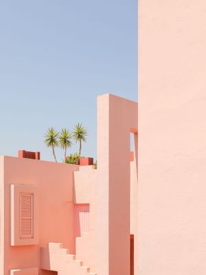 Palm trees rise from a pink modernist building with geometric shapes and steps.