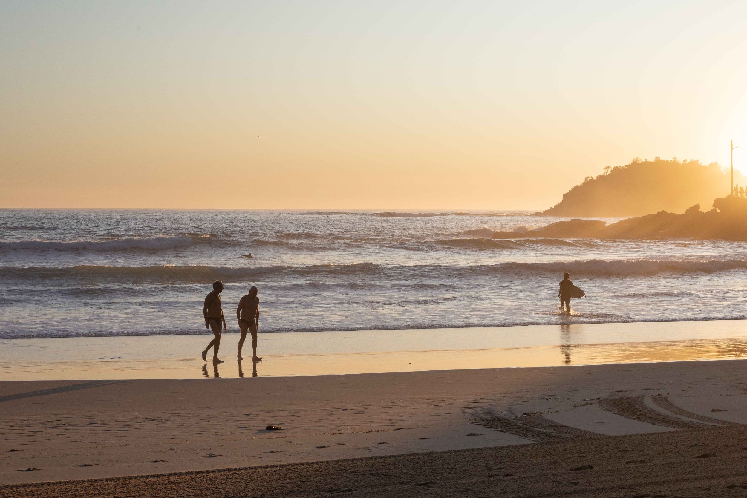 Silhouettes of beachgoers walking along shoreline at golden sunset.