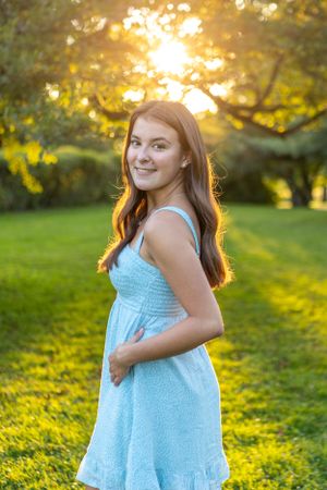 Summer portrait in a blue dress with golden sunset backlighting through trees.