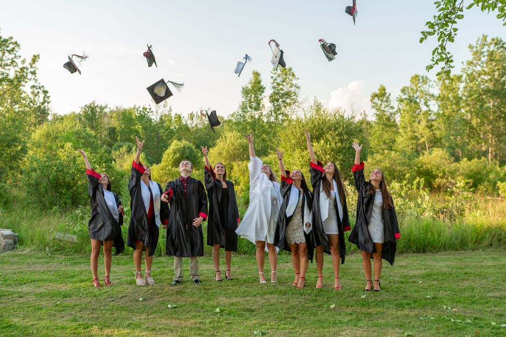 Graduates throw their caps in the air during a celebration photo against trees at sunset.
