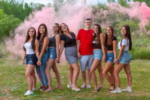 Group of friends posing outdoors with vibrant pink smoke effects in a summer setting.