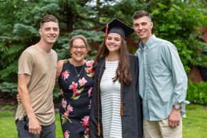 A graduation celebration photo with family members outdoors against green trees.