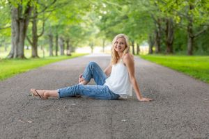 Person in casual summer attire sitting on a tree-lined path.