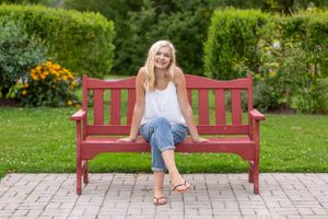Person relaxing on a red wooden bench in a garden with colorful flowers.