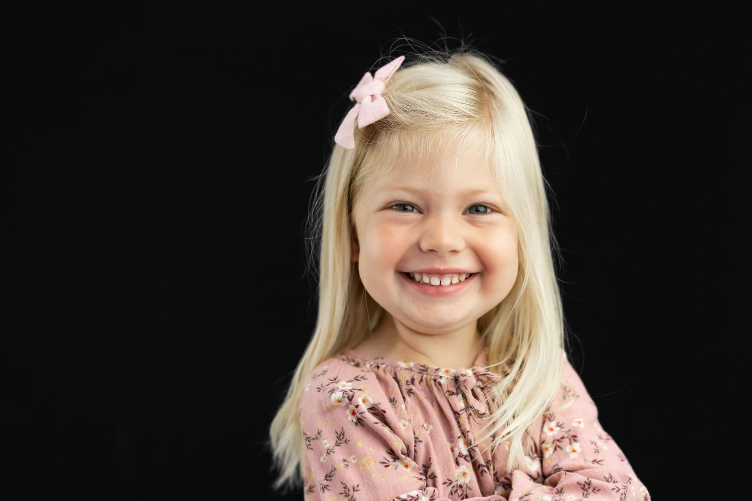 smiling blonde girl with light pink bow