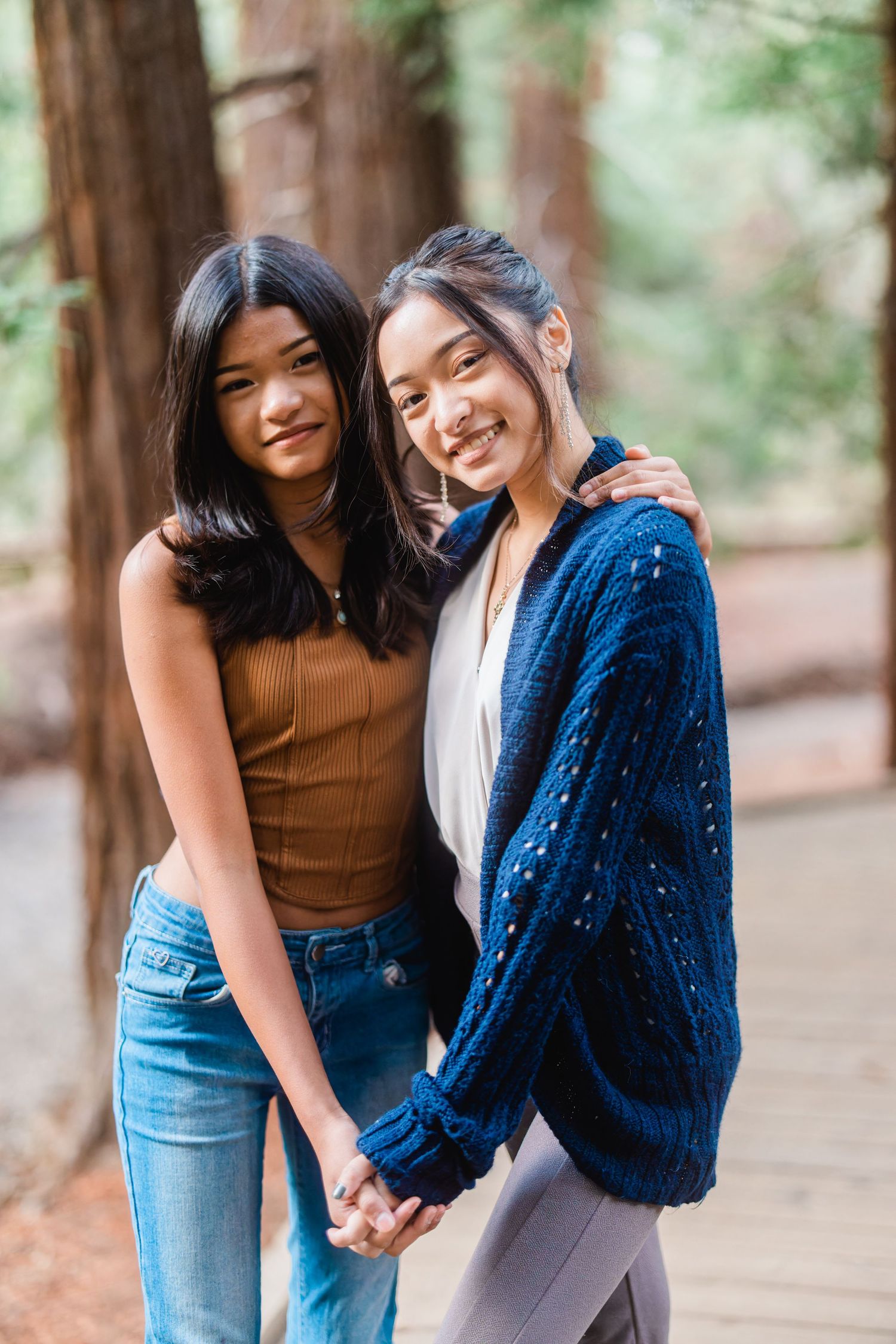 Two friends embracing and smiling together in a redwood forest setting.