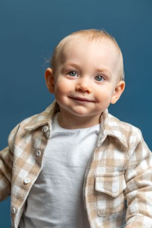 Close-up portrait of smiling baby wearing plaid shirt against blue background.