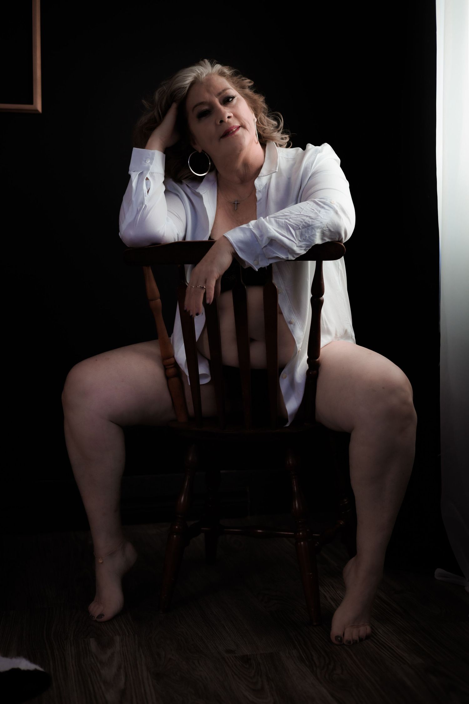 Artistic portrait of woman in white shirt seated on wooden chair.