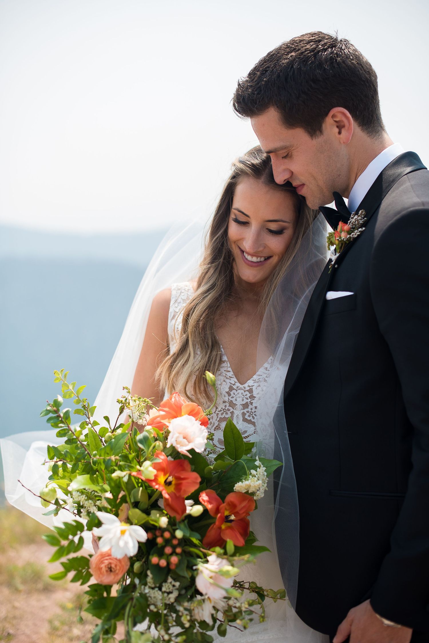 bride and groom look at a luxurious floral bouquet of orange and green flowers on a mountaintop in Vail, Colorado