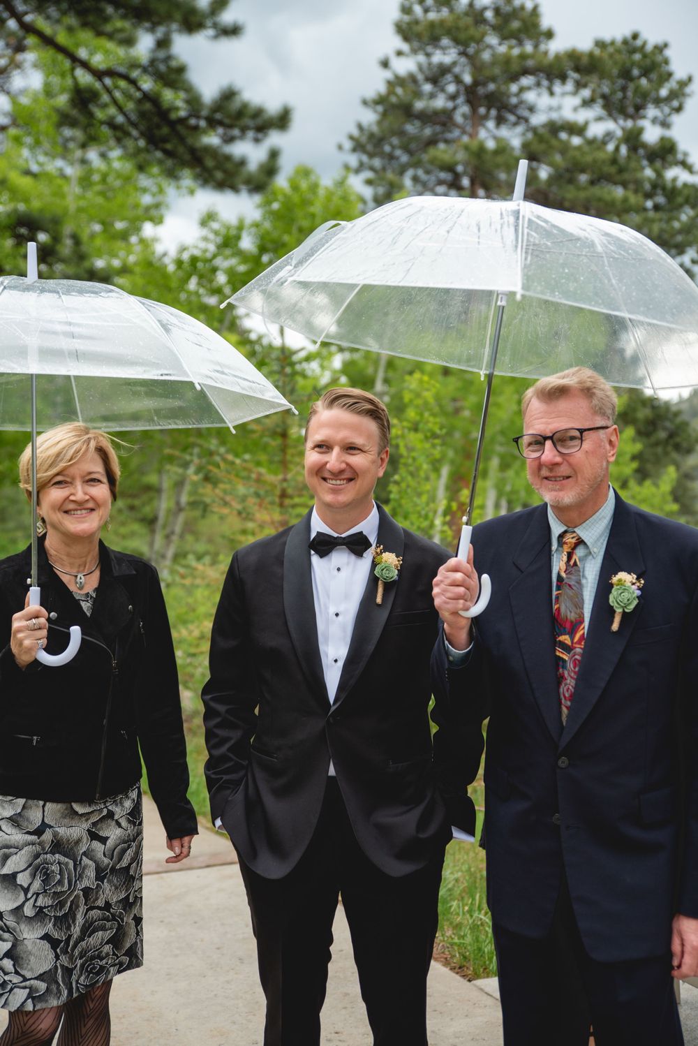 Groom with his parents, standing under her umbrellas waiting for rain to stop