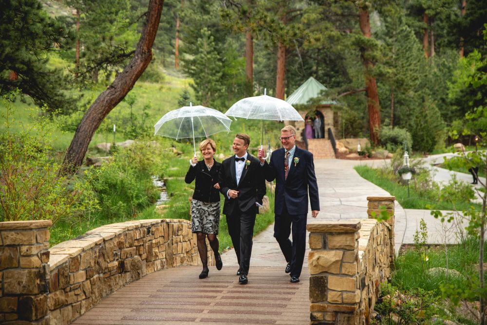 Groom and parents walking down the aisle under umbrellas