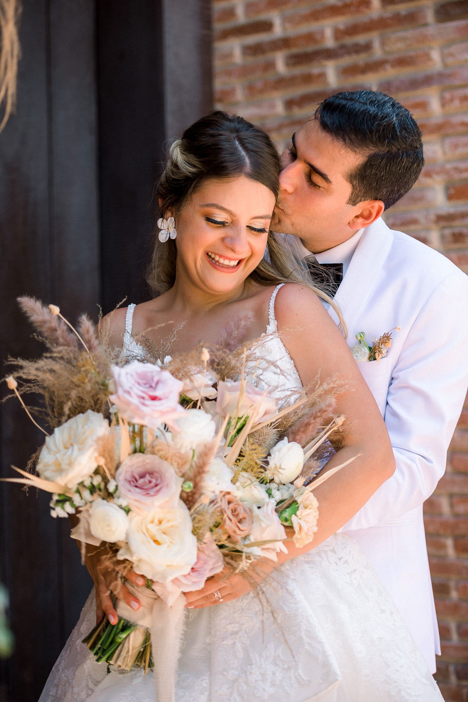 A bride holding a romantic bouquet of blush and cream flowers shares an intimate moment.