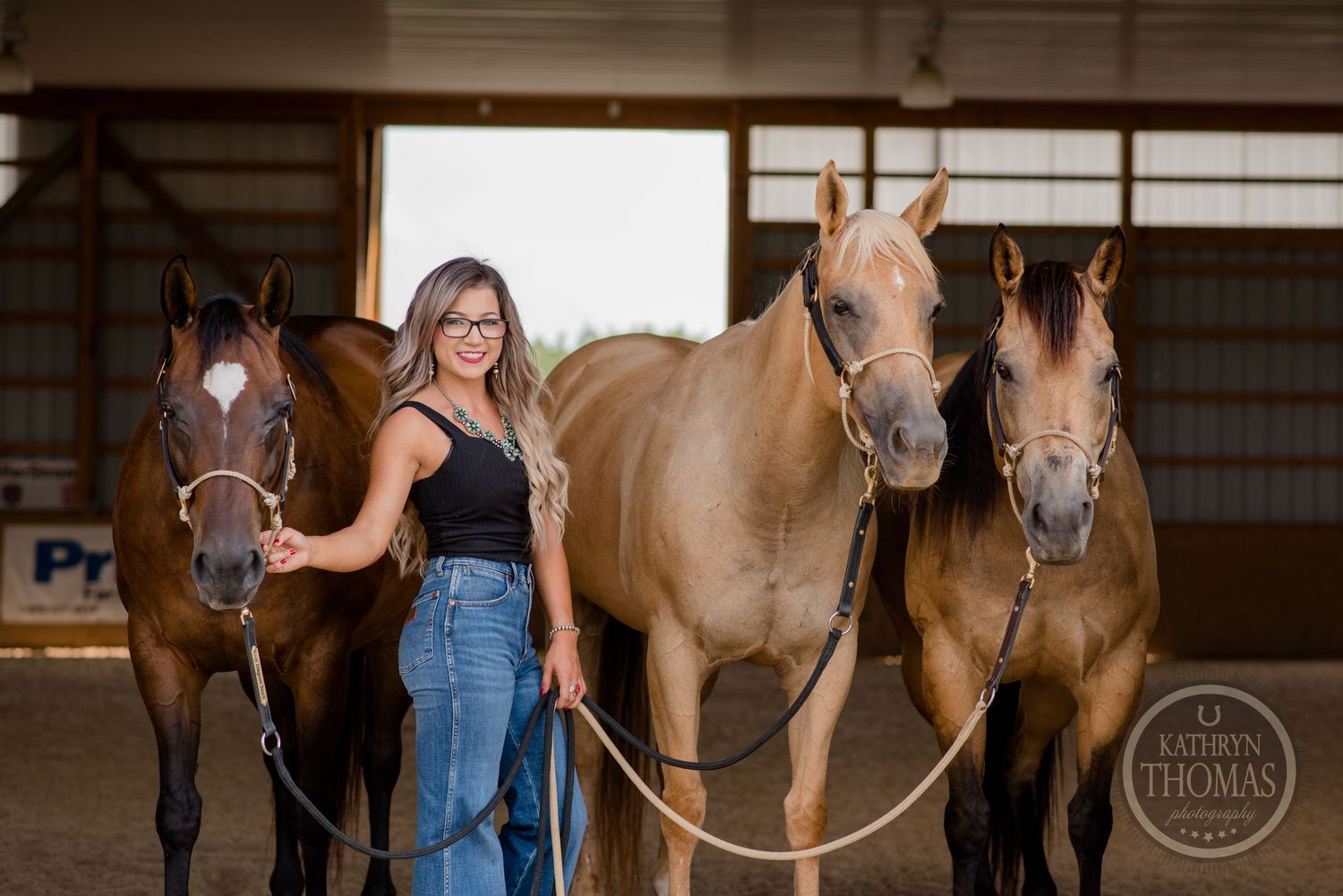 Three horses stand together in an indoor arena with their handler.