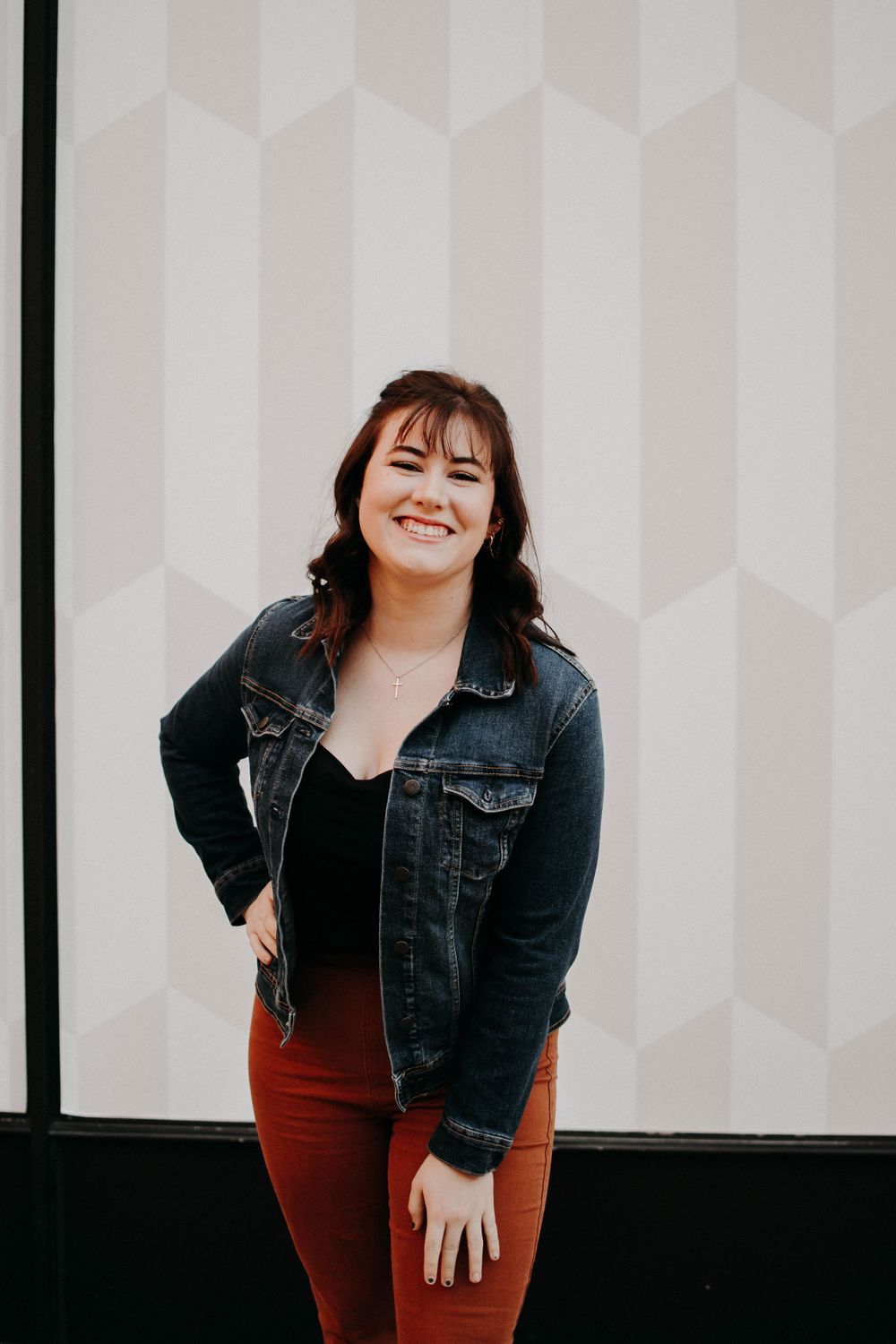 Casual urban fashion look with denim jacket and rust-colored bell bottom pants against white wall.