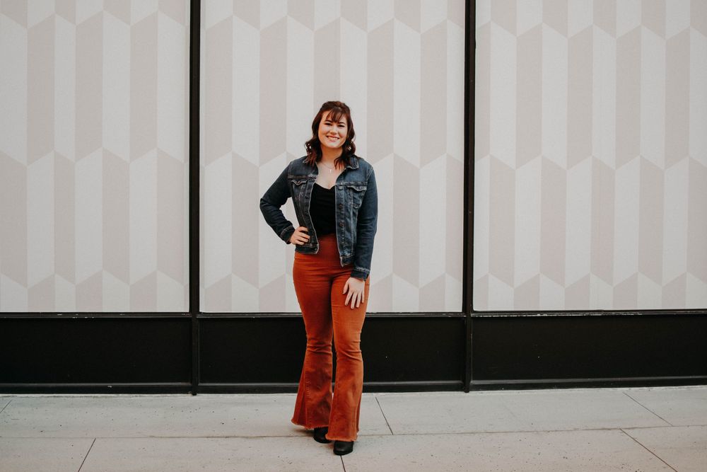 Stylish outfit featuring red flared pants and denim jacket against geometric patterned wall.